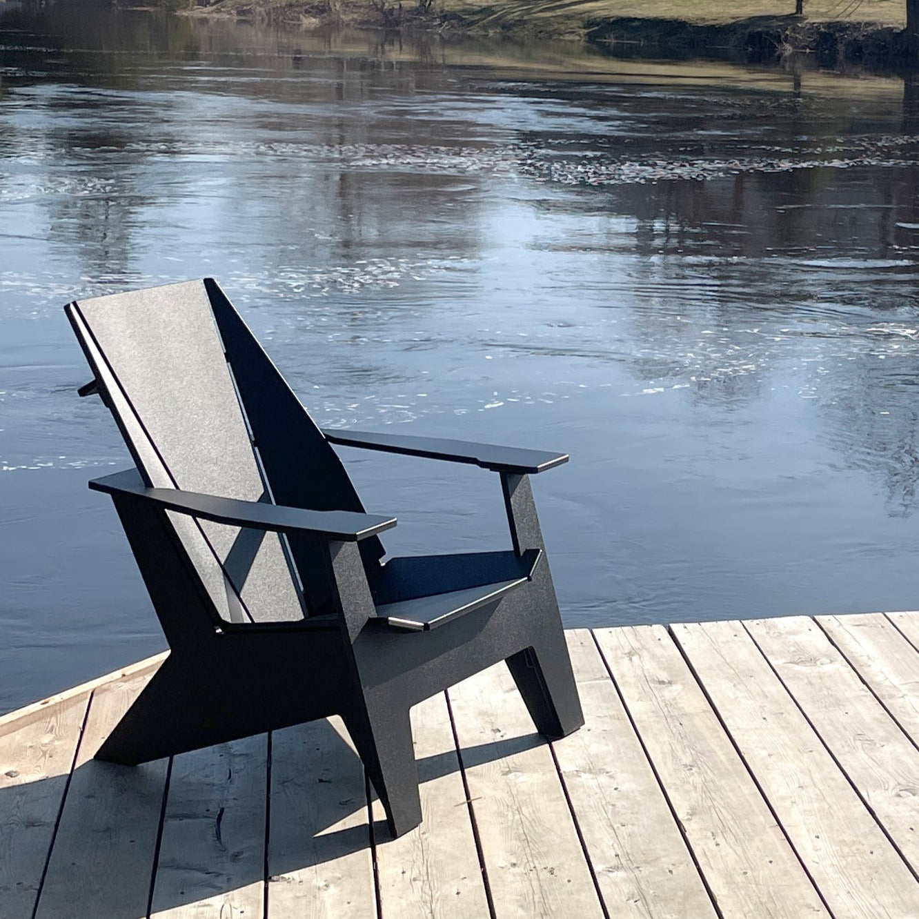 Shot of summer lake in Canada, Ori Muskoka chair is sitting on grey, cedar deck with water in the background.