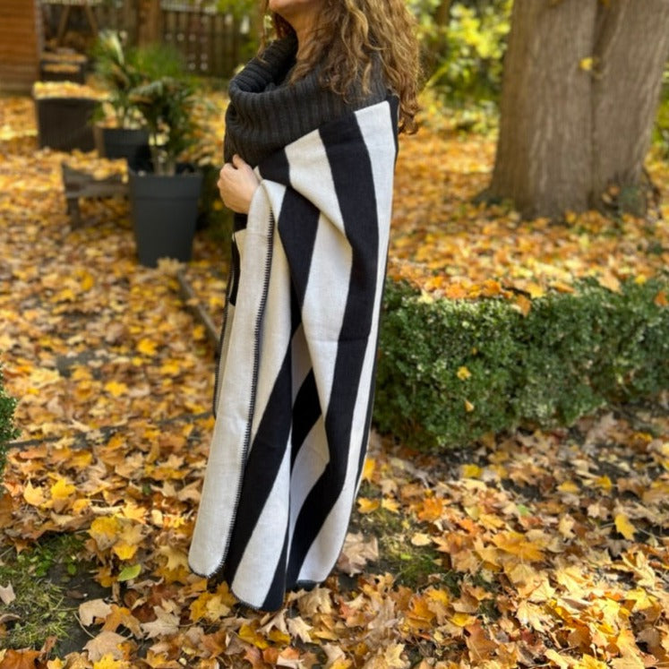 Shot of woman wearing the Snowden Cotton Blanket in a garden in fall, surrounded by garden full of leaves.