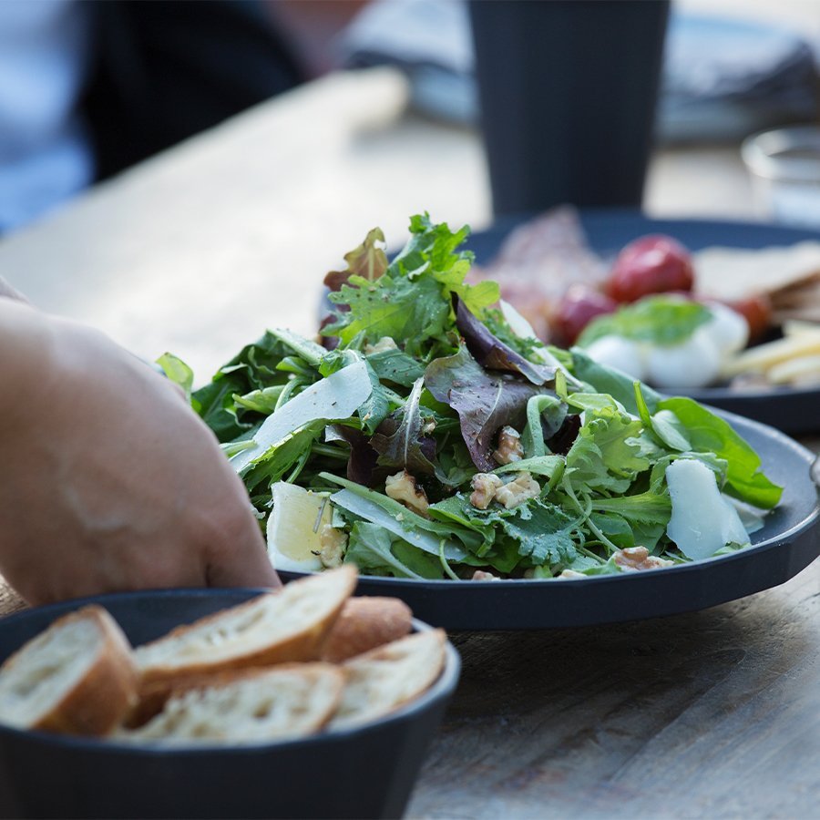 
                  
                    Close up shot of leafy salad on a large black, bamboo plate which is featured on an outdoor table.
                  
                
