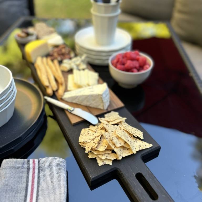 
                  
                    Paddle serving board in blackened oak with Charcuterie outdoors.
                  
                