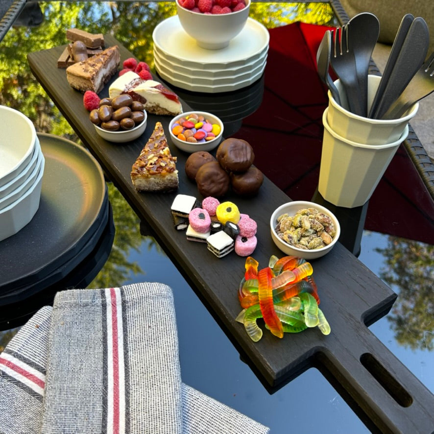 Paddle serving board in blackened oak with a mixture of desserts outdoors.